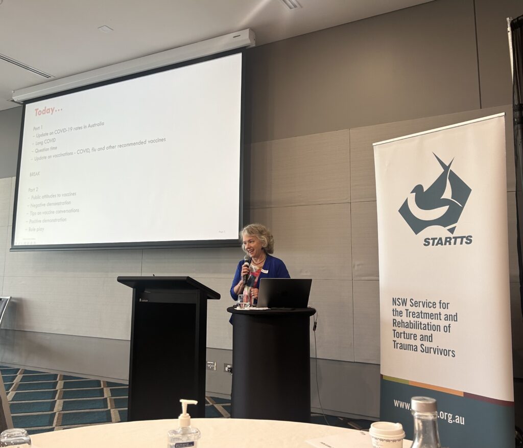 Photograph of Julie Leask holding a microphone, presenting at the STARTTS (NSW Service for the Treatment and Rehabilitation of Torture and Trauma Survivors) workshop.